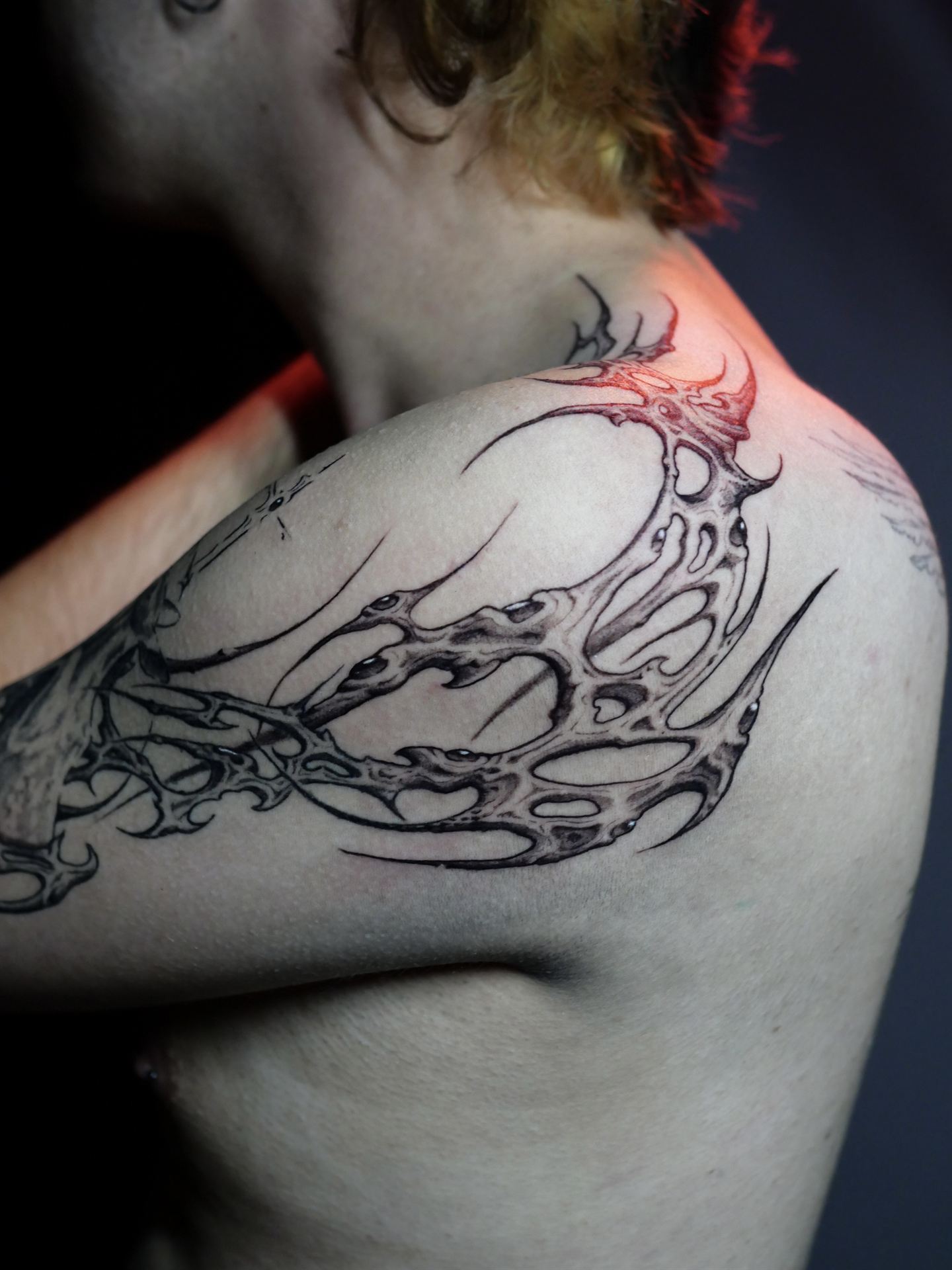 Pieza orgánica de hombro tatuada por Mecha, iluminada con luz roja