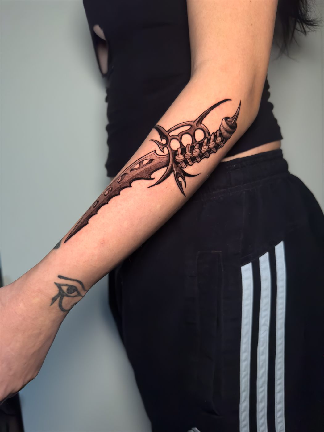 Daga de hueso y columna tatuada a lo largo del antebrazo